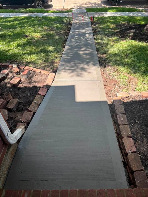 Concrete front walk leading to the street between brick edging and grass