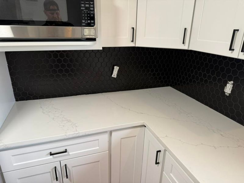 Finished black hex tile backsplash above a white quartz counter and white cabinets