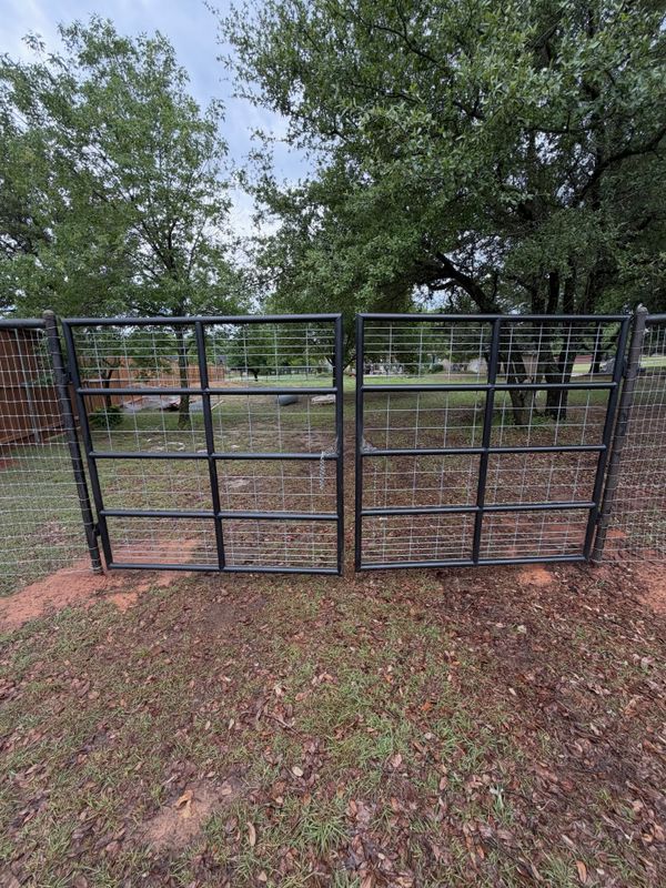 Black steel pipe entry gate set between mature trees on a Texas ranch