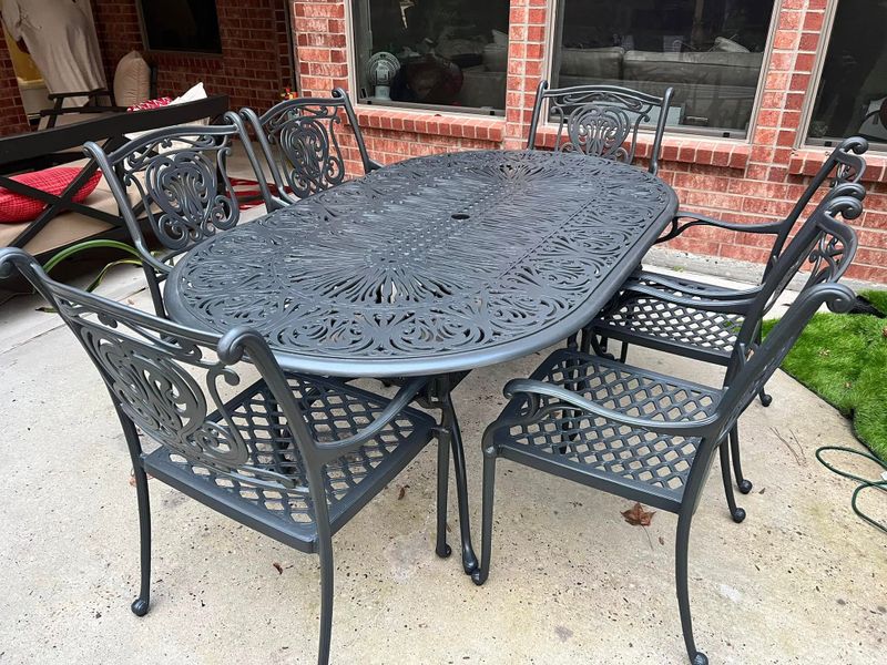 Dark gray cast-metal oval patio table with six scrolled chairs on a covered patio