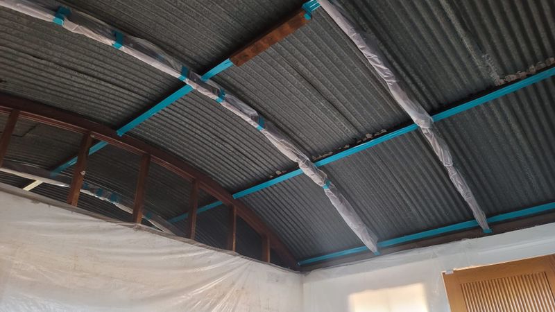 Metal roof with fresh spray foam applied between blue framing