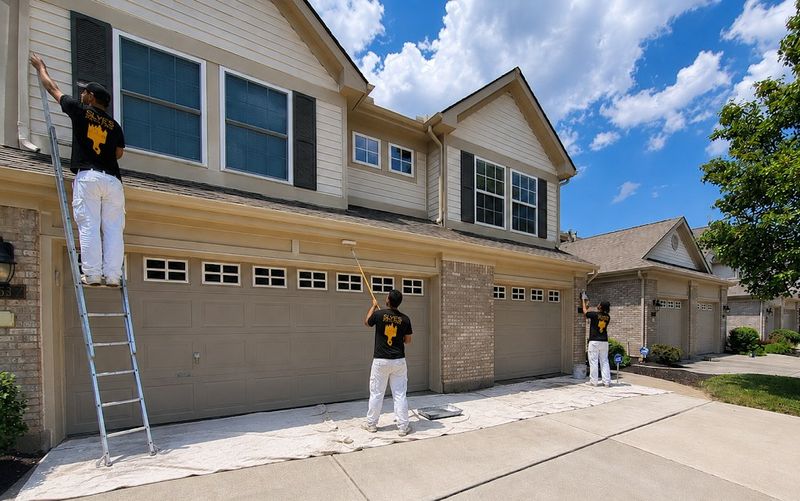 Slye's Painting crew painting garage doors on a townhome with a ladder and drop cloths