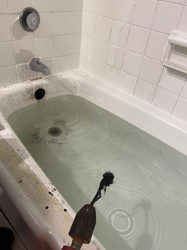 Tub full of standing water with a drain tool in place