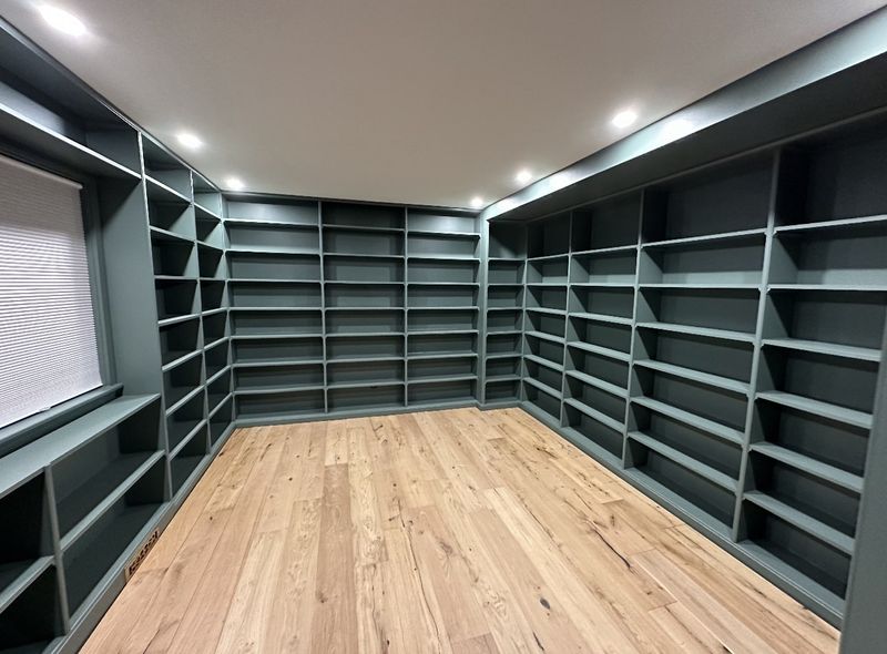 Custom built-in shelving painted deep green along two walls of a room with a light wood floor