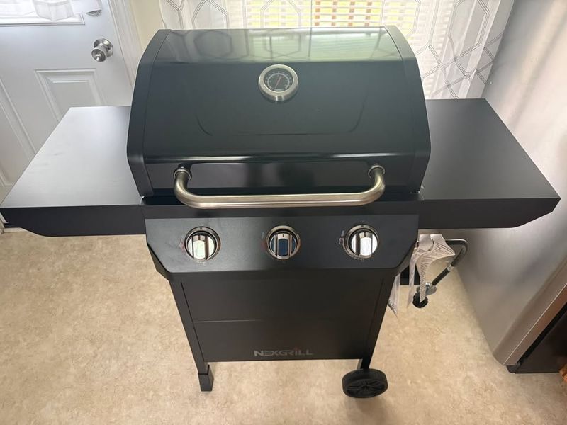 Assembled three burner gas grill with side shelves on the same vinyl floor