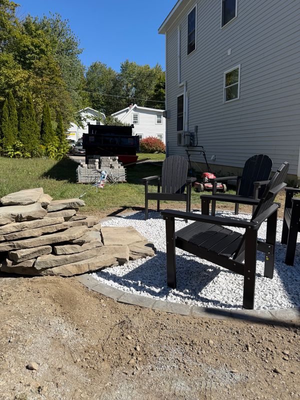 The yard before the work, with stone stacked and furniture sitting on bare ground