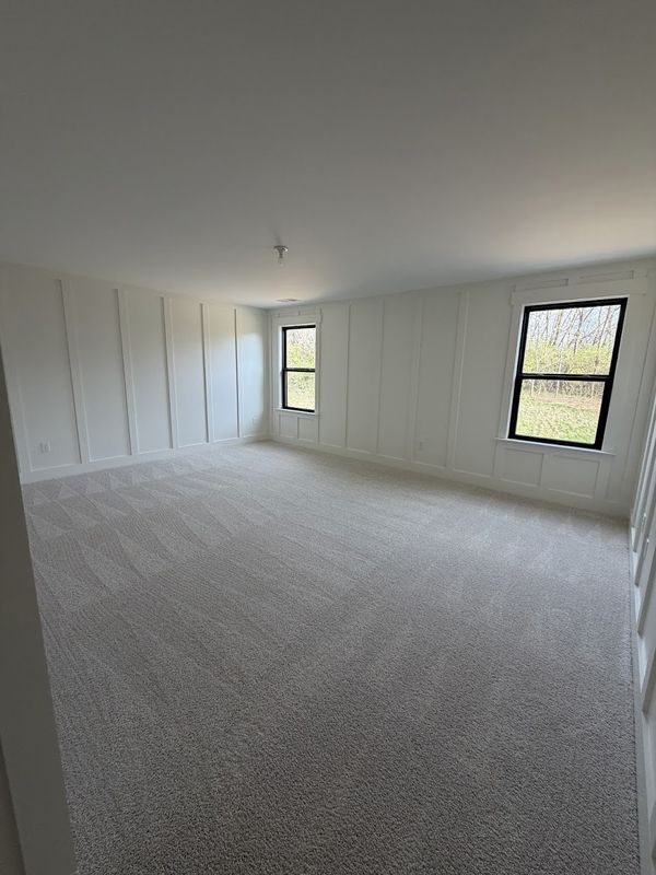 Floor-to-ceiling board and batten walls in white in an empty carpeted room with two windows