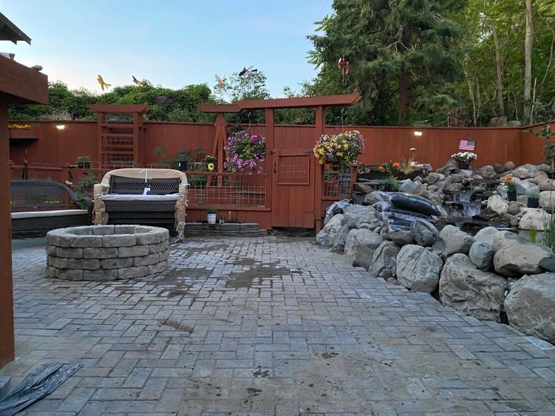 Finished paver patio with a round fire pit, seating and a boulder water feature
