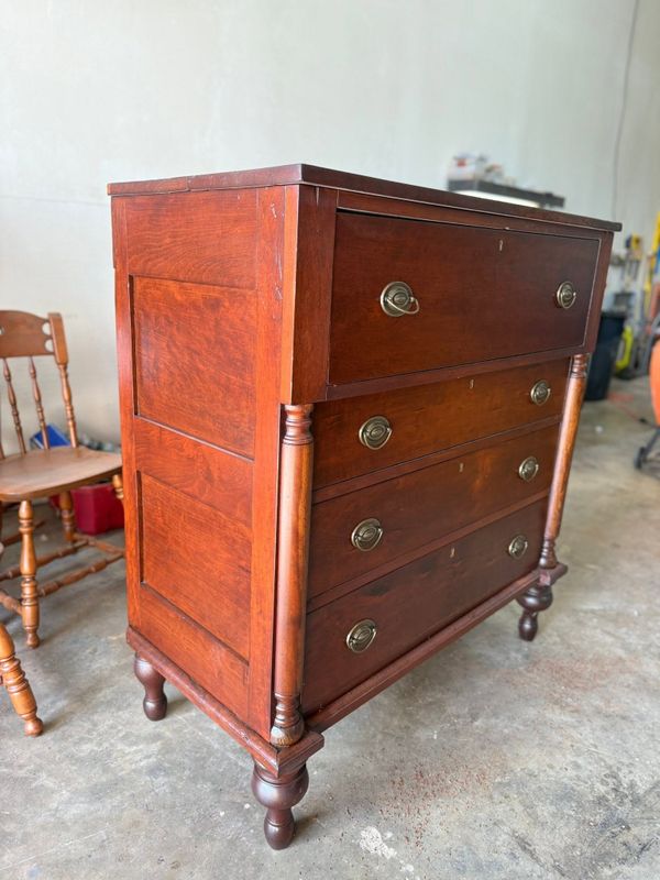 Tall wooden chest of drawers with round brass pulls in the workshop