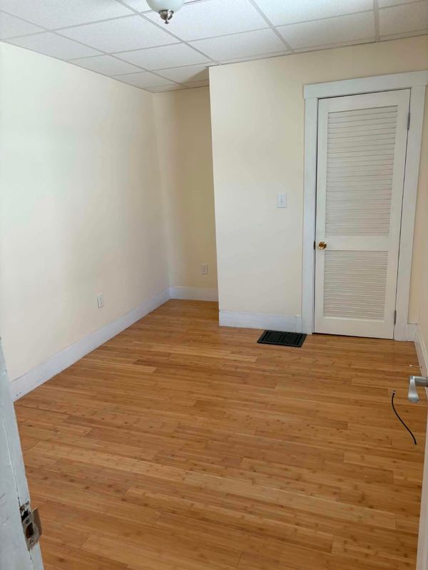 Room with cream walls, white baseboards and a white louvered door above a wood floor