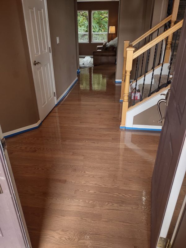 Glossy refinished red-brown oak hallway beside staircase, a hardwood floor refinishing project