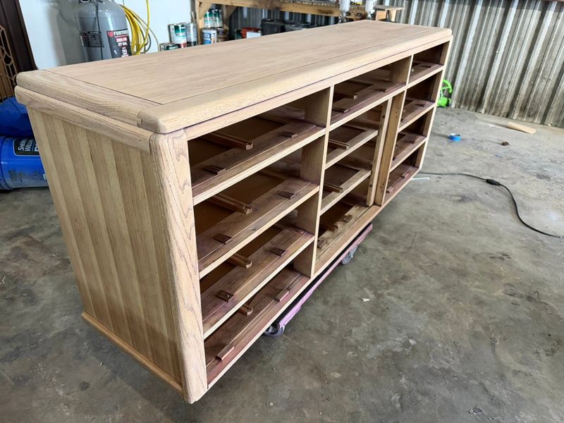 Pale, unfinished wood cabinet with open shelves on dollies in the workshop