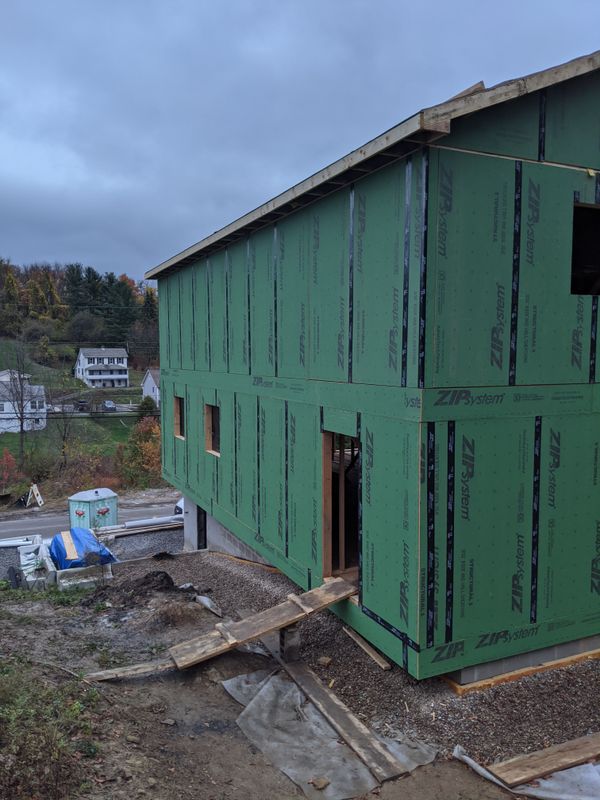 Green-sheathed house frame seen from the side with a porch footing