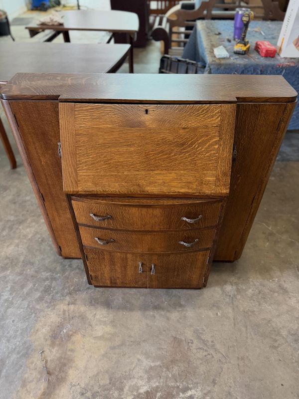 Oak bureau with a drop-front writing desk and curved drawers with metal pulls, standing in a workshop