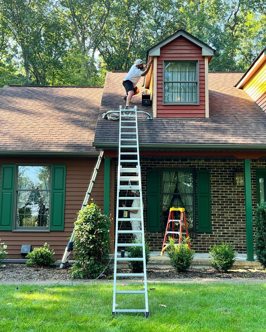 Painter on a tall ladder painting a dormer