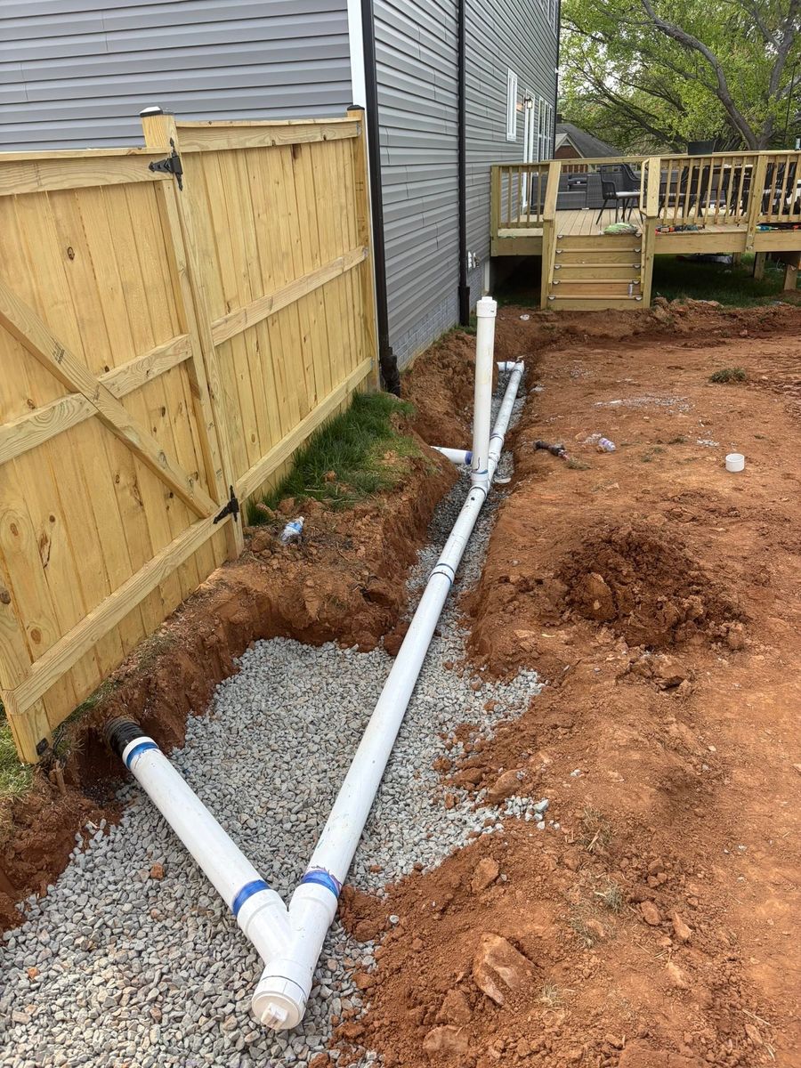 White drain pipe being laid in a trench beside a house
