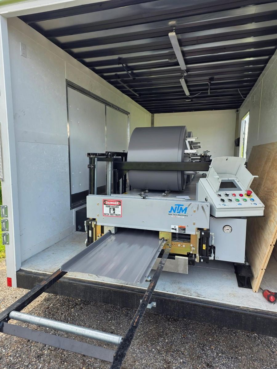 Roll forming trailer open on site, forming a grey standing seam panel to length