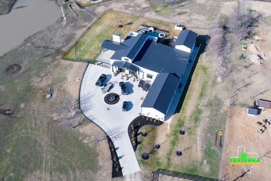 Aerial view of a large modern farmhouse with new hardscape and fresh lawn