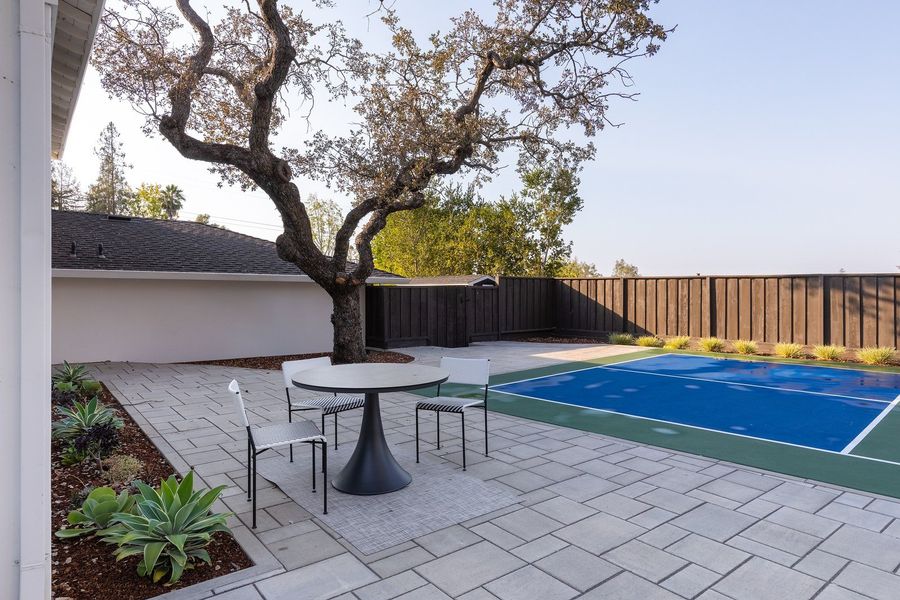 Round bistro table and chairs on grey pavers with agaves, an old oak and a dark fence