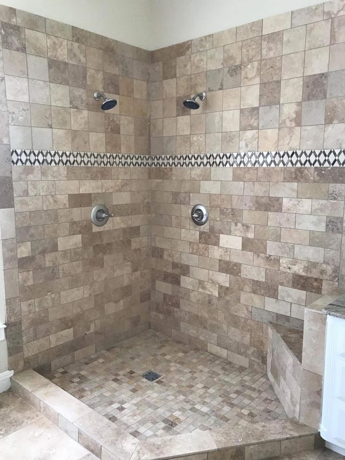 Stone-look tiled shower with two shower heads and a mosaic band