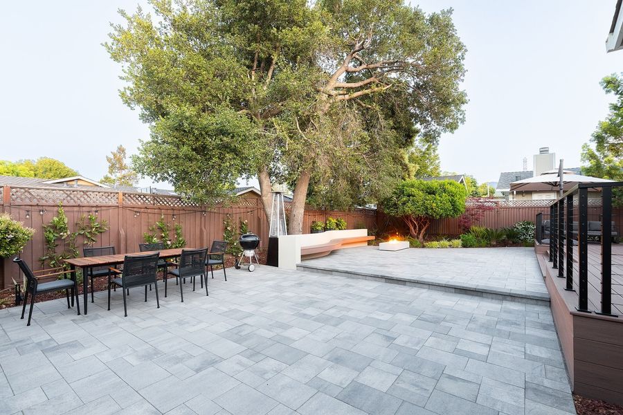Dining table with black chairs on the paver court, with the deck and cable railing at right