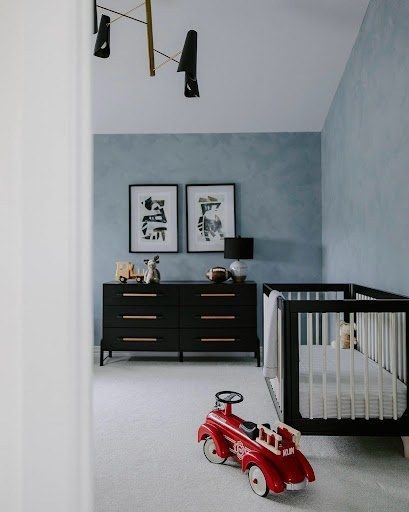 Soft blue Roman clay accent walls in a nursery with a black crib and dresser