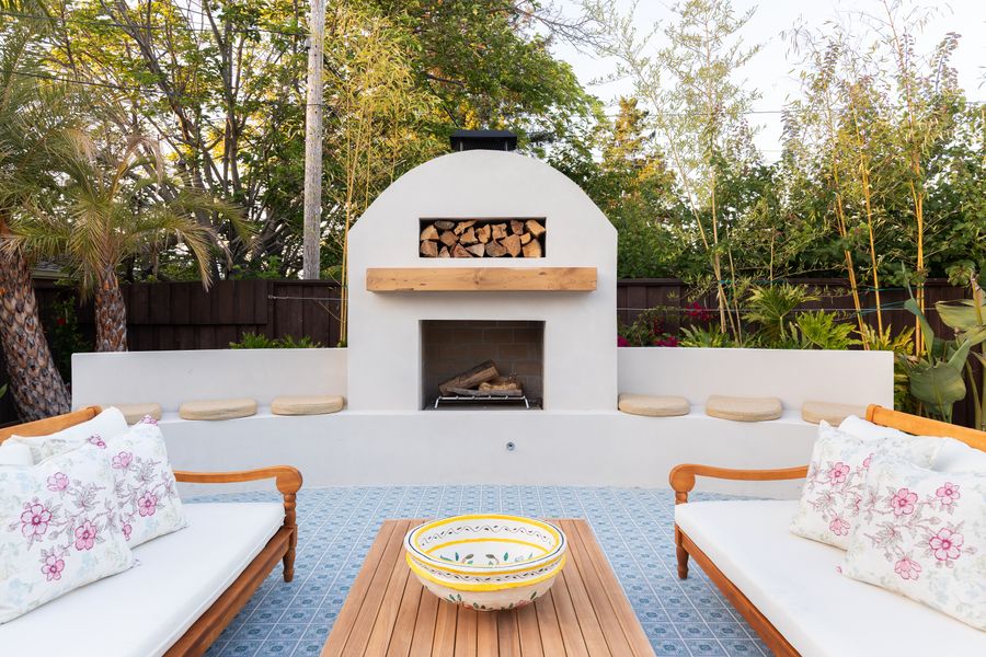 Arched rendered fireplace with a timber mantel and log store, timber sofas facing it across a low table
