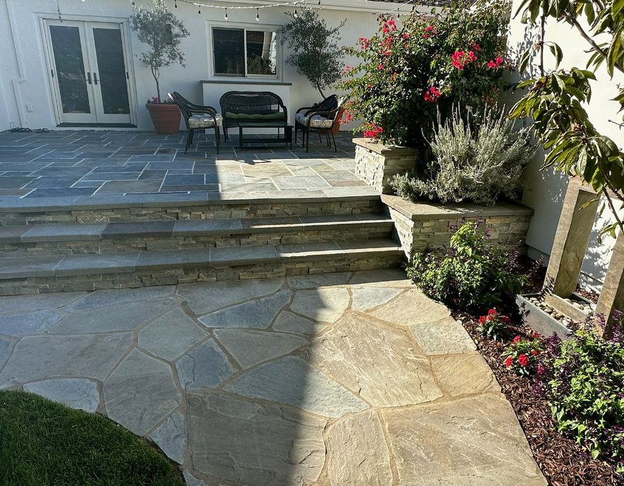 Straight flight of stacked-stone steps with bluestone caps between irregular flagstone paving and a cut-stone patio, a stone planter with lavender, bougainvillea and a slim stone water feature.