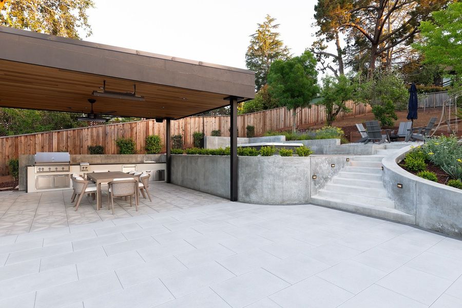 Pavilion and outdoor kitchen beside the concrete stair, with a curved planter wall and fire court above