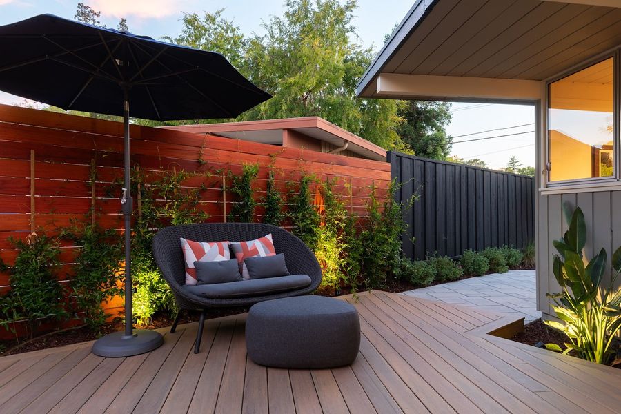 Entry court at dusk with concrete stepping pads set in dark river rock, lit ornamental grasses and a wood-look deck