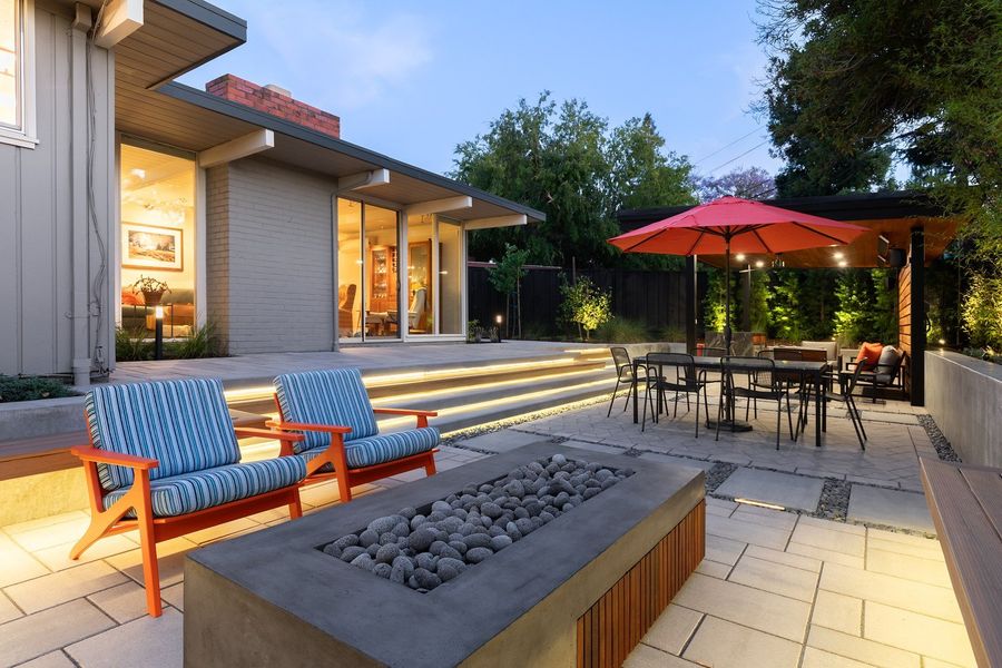 Concrete fire table with a wood-slat side and lava stones, orange and striped lounge chairs and lit steps behind