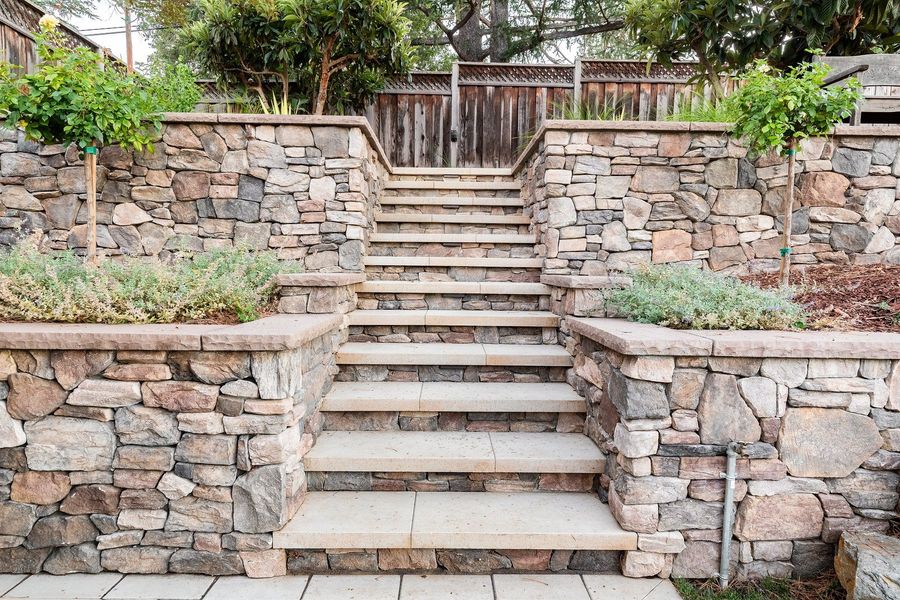 Wide flight of stone steps rising between two stacked-stone walls, each wall topped with a planter of silvery herbs