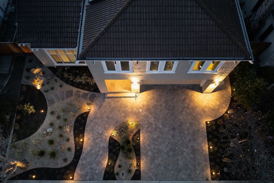 Aerial dusk view of the front court, warm-toned pavers divided by curving gravel beds with grasses, boulders and low lights