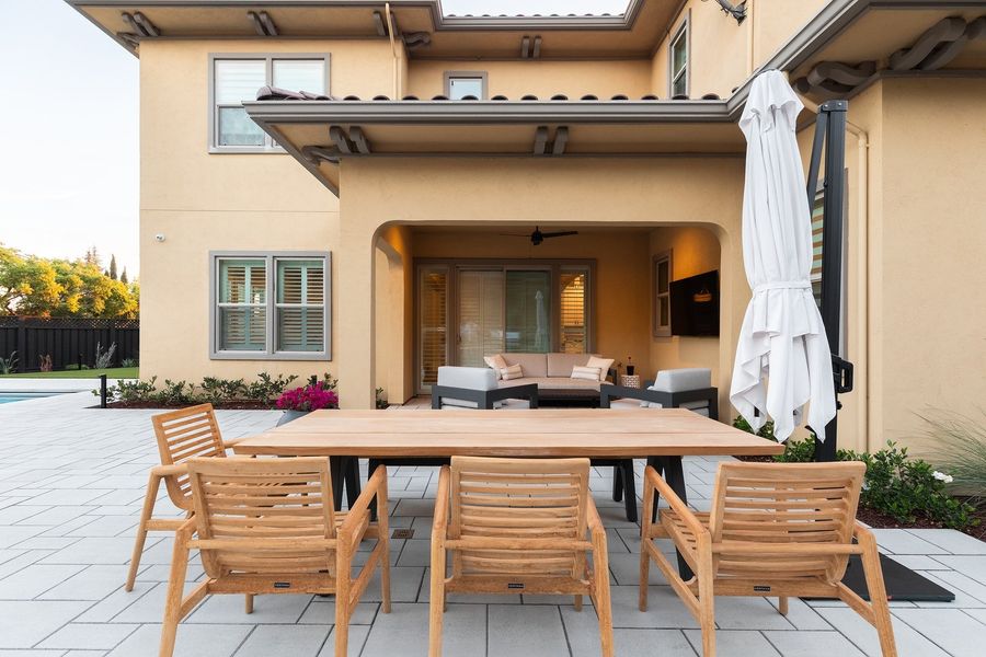 Covered patio with dining table and chairs under a closed umbrella and seating beyond on light pavers