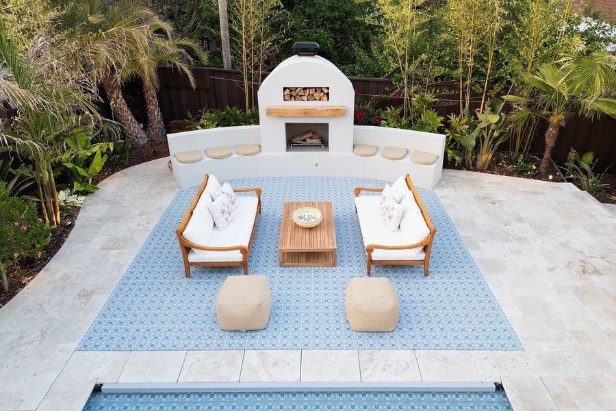 Straight-down aerial of the tiled lounge, two daybeds and poufs, a curved seat wall and fireplace set in a travertine terrace