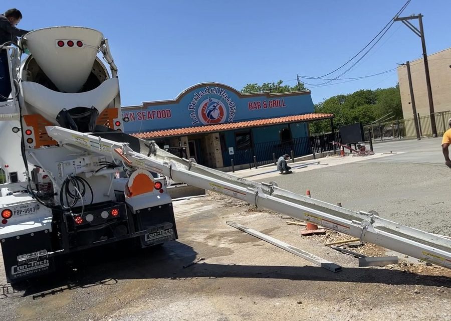Concrete mixer truck with its chute extended placing a commercial slab in front of a San Antonio storefront
