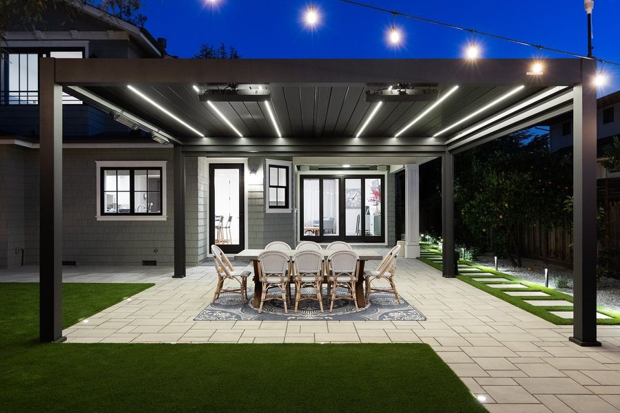 Straight-on night view of the lit pergola over a dining table with turf in front and stepping pads beside the house