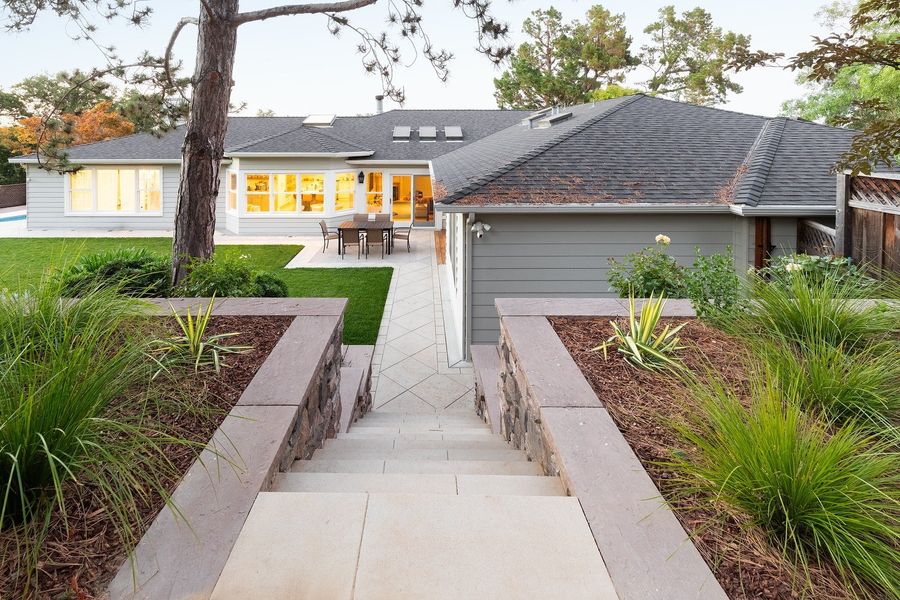 Looking down a paved stair between two stone-capped planters of grasses toward the back of the house at dusk