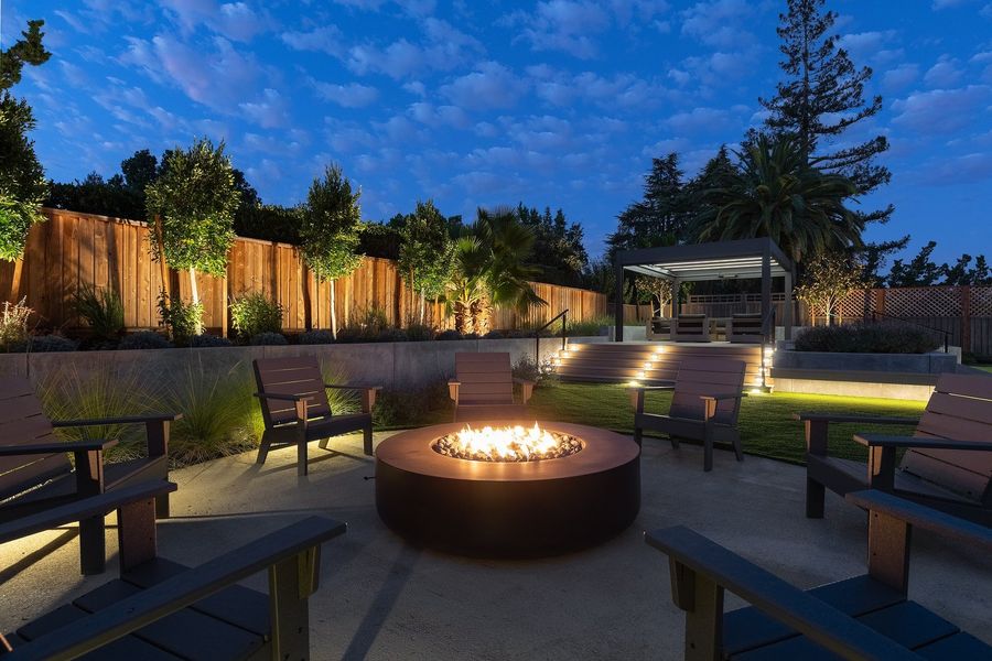 Gas fire bowl glowing at night with chairs around it and lit steps in the background