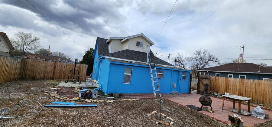 Blue cottage partway through an exterior repaint with the yard around it