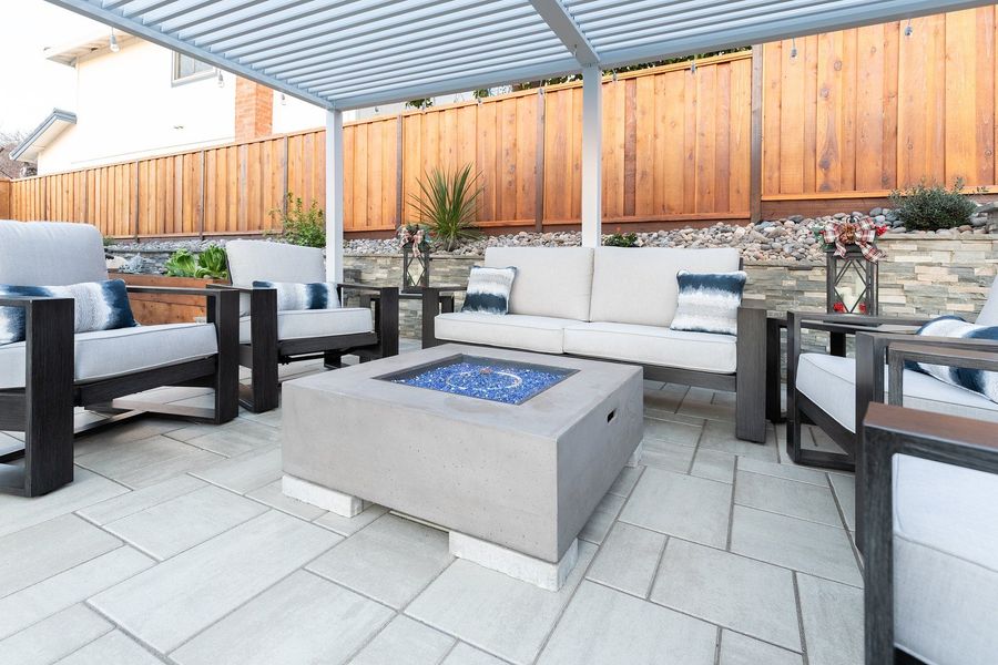 Close view of the fire table filled with blue glass between low sofas on pale pavers, with a stone wall behind