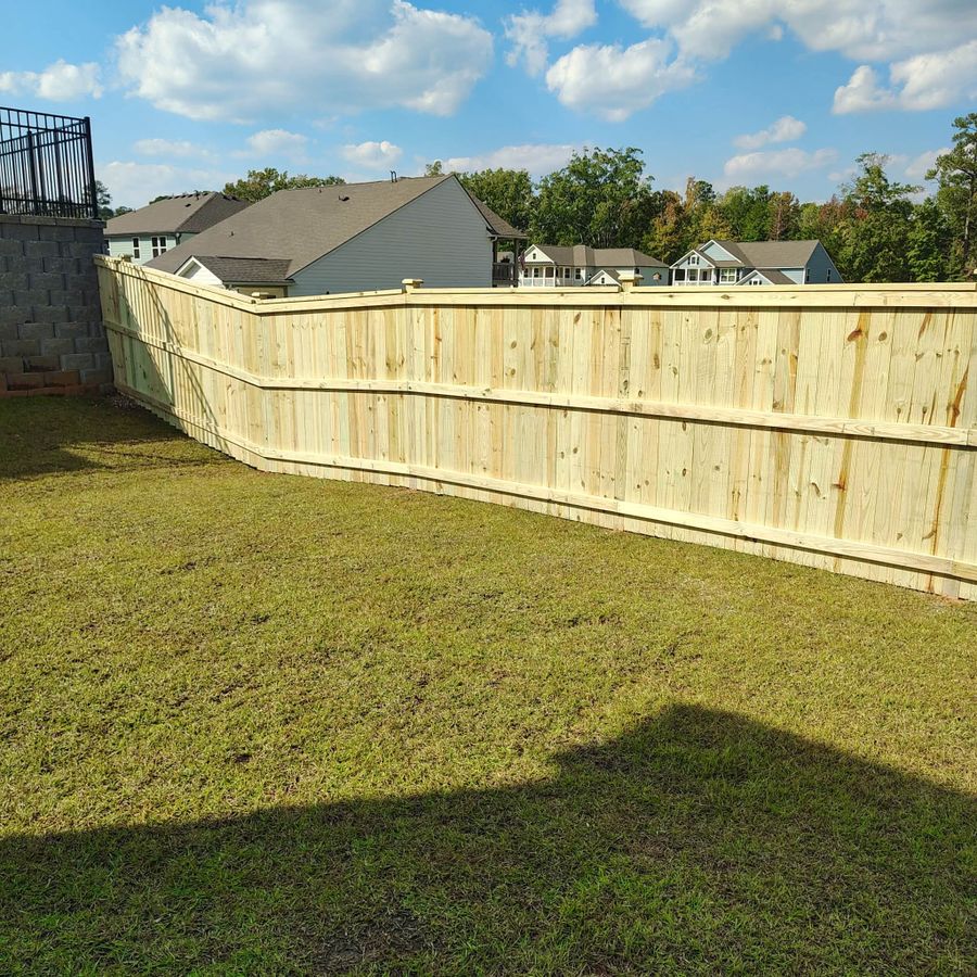 Pressure treated wood privacy fence running across a sunny backyard