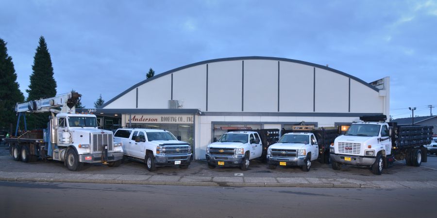 Anderson Roofing truck fleet parked in front of the company shop at dusk