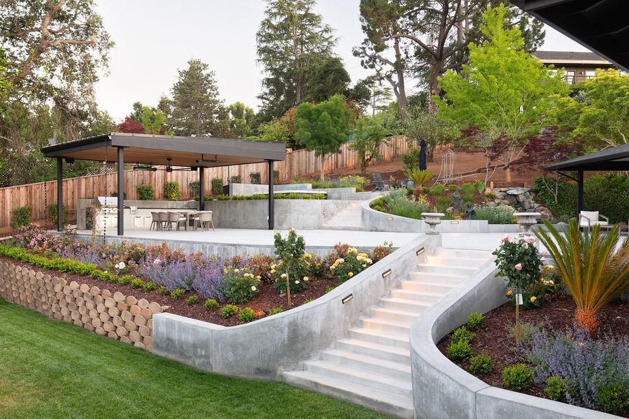 Curving concrete stair and low wall beside layered planting, with the pavilion on the upper terrace