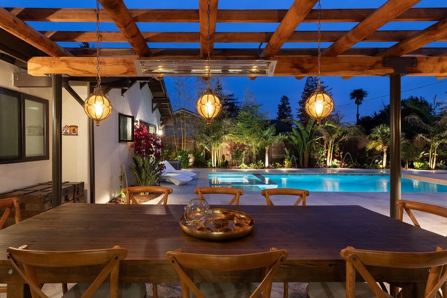 The pergola dining table at dusk with lit glass lanterns, uplit palms and bougainvillea behind