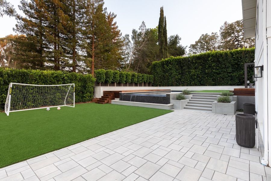 Grey paver terrace beside a green lawn leading to a stepped concrete wall with planters and a hardwood deck at the top
