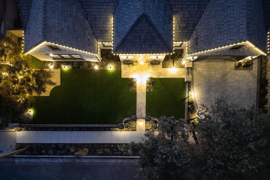 Night aerial looking straight down at the lit front garden, glowing entry walk, lawn and roofline lights