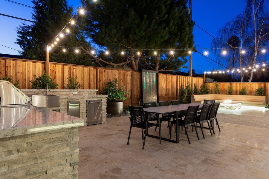 Night view of the dining table and stacked-stone kitchen island, with the fire bench glowing at the far end of the yard
