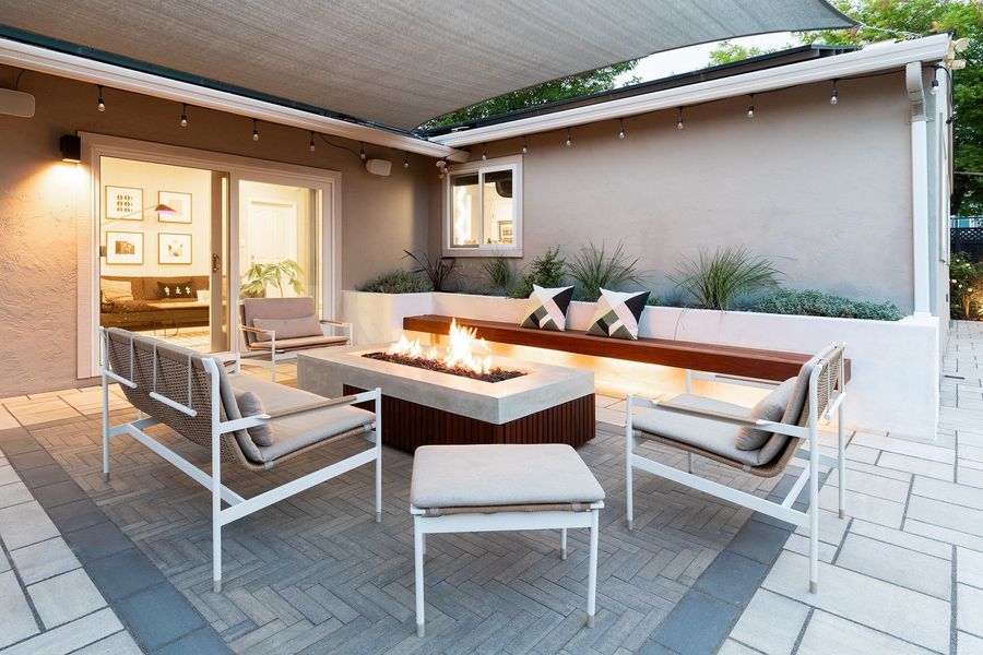 Daytime view of the fire table, built-in ipe bench, planter and white-framed outdoor sofas on grey herringbone pavers