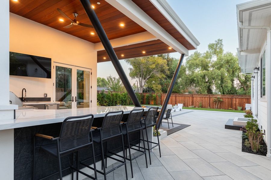 Bar-height counter with four black stools and a veined stone top, with the kitchen and paving beyond at twilight